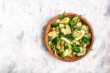 Avocado salad with broccoli, cucumber and boiled eggs in a white vintage bowl. Delicious breakfast or snack on a light background, top view