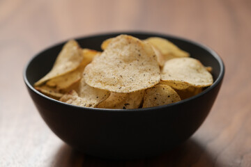Organic potato chips with black pepper in black ceramic bowl on walnut wood background