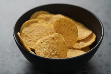 Round nachos in black ceramic bowl on concrete background