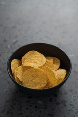 Round nachos in black ceramic bowl on concrete background with copy space