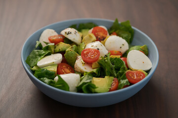Salad with avocado, cherry tomatoes, romaine and mozzarella in blue bowl on walnut table
