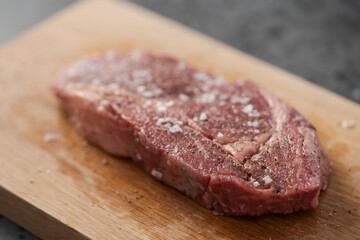 Raw ribeye steak spiced and ready to cook on oak board