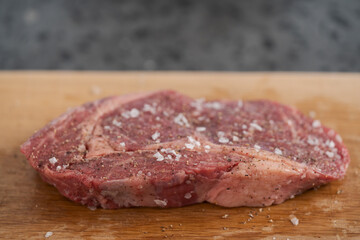 Raw ribeye steak spiced and ready to cook on oak board