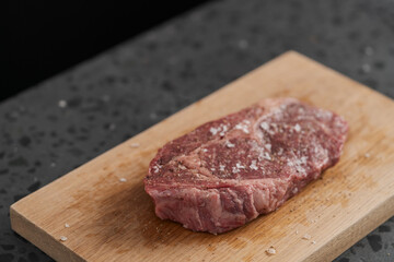 Raw ribeye steak spiced and ready to cook on oak board