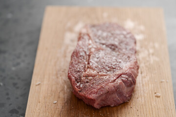 Raw ribeye steak spiced and ready to cook on oak board