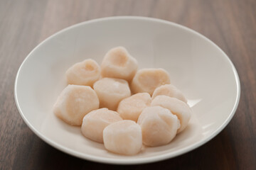 frozen scallops in white bowl on walnut table for defrosting