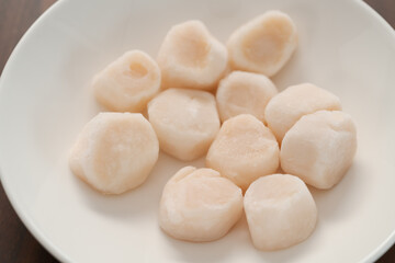 closeup of frozen scallops in white bowl on walnut table for defrosting