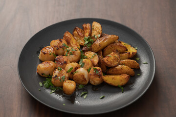 roasted scallops with baked potatoes wedges on a black plate on walnut wood background