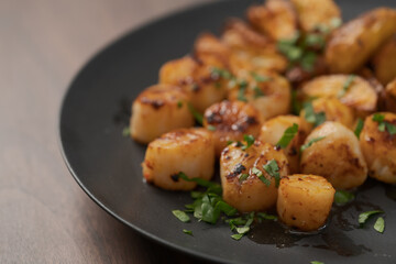 roasted scallops with baked potatoes wedges on a black plate on walnut wood background