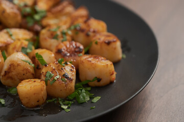 roasted scallops with baked potatoes wedges on a black plate on walnut wood background