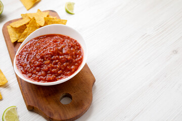Homemade Tomato Salsa and Nachos on a rustic wooden board on a white wooden background, side view. Copy space.
