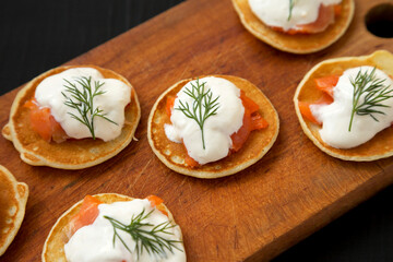Homemade Blini with Smoked Salmon, Creme and Dill on a rustic wooden board on a black background, side view. Close-up.