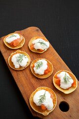Homemade Blini with Smoked Salmon, Creme and Dill on a rustic wooden board on a black background,...