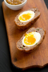 Homemade Scotch Eggs on a rustic wooden board on a black surface, side view. Close-up.