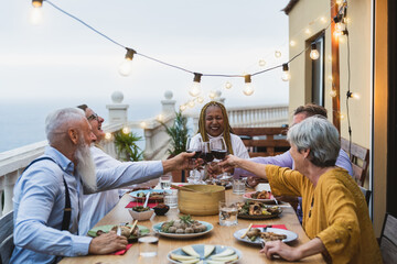 Happy multiracial seniors toasting with red wine glasses together on house patio dinner - Elderly...