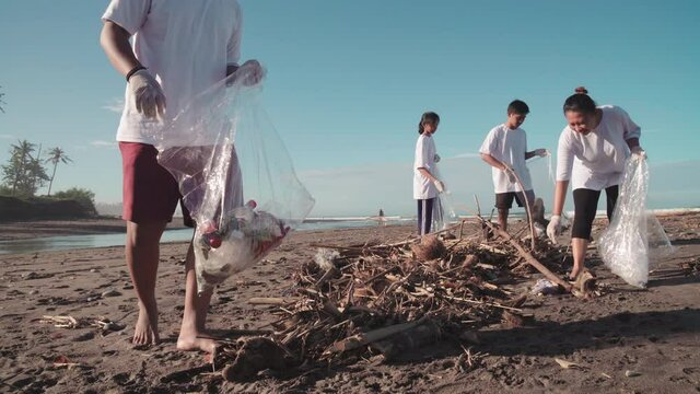 Full shot of one of most polluted beach filled with dirty sand, twigs, litter and group of local environmentalists in white t-shirts picking up garbage cleaning area