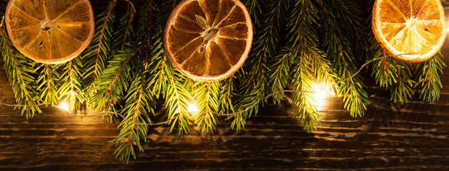 Christmas background with fur-tree branches, dried oranges and led garland on wooden background....
