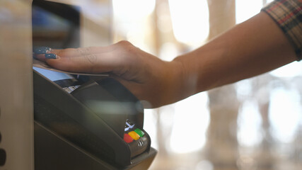 Close up hands of woman making payment with credit card machine terminal. Woman paying with contactless credit card with NFC technology. Wireless money transaction. Wireless payment