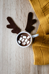 Eine Tasse heiße Schokolade mit Marshmellows und ein Rentier Geweih auf braunen Filz au einem Holztisch. Gelbe Wolldecke, Symbol, Weihnachten.