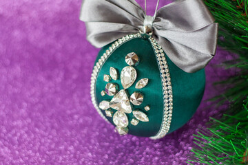 Green Christmas ball in rhinestones for decorating the Christmas tree. Christmas toy. Christmas toy for decorating a Christmas tree on a lilac background. Shining crystals on a green ball.