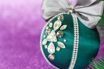 Green Christmas ball in rhinestones for decorating the Christmas tree. Christmas toy. Christmas toy for decorating a Christmas tree on a lilac background. Shining crystals on a green ball.