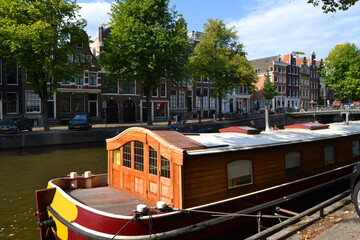 Fototapeta na wymiar A houseboat in foreground. The canal and facades of houses in background. Amsterdam, The Netherlands.