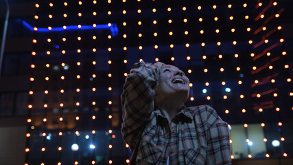 Young woman is very emotionally looking at glowing houses on the street of the evening city admires the beauty of buildings