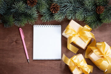 Christmas gifts, fir branches and a notebook for notes on a dark wooden background. Winter Christmas holiday theme. Flat lay, top view. Copy space for text.