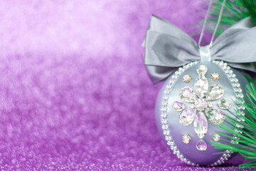 Grey Christmas ball in rhinestones for Christmas tree decoration. Christmas toy. Christmas toy for decorating a Christmas tree on a lilac background. Shining crystals on a gray ball.