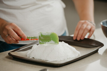 А close photo of the hands of a young woman who is improving with a scapula a shape of a big meringue on a tray. A girl is preparing to cook a delicious lemon meringue tart.