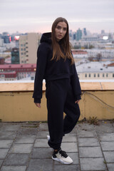 Full height photo of young woman, standing on roof of tall building in large city.