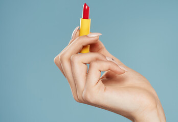 Woman holding lipstick in hand on blue background cropped view of model