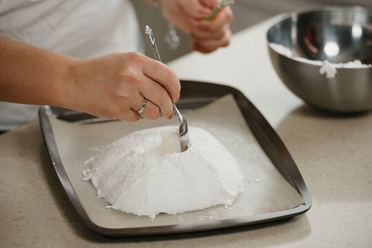 А close photo of the hands of a young woman who is creating with a spoon a form of a giant meringue on a tray. A girl is preparing to cook a delicious lemon meringue tart.