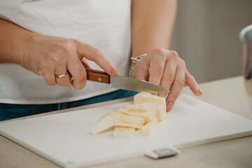 Obraz na płótnie Canvas А close photo of the hands of a young woman who is cutting fresh farm butter on a cutting board with a sharp knife.