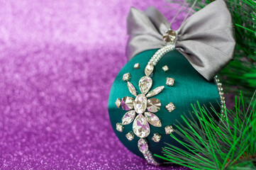 Green Christmas ball in rhinestones for decorating the Christmas tree. Christmas toy. Christmas toy for decorating a Christmas tree on a lilac background. Shining crystals on a green ball.