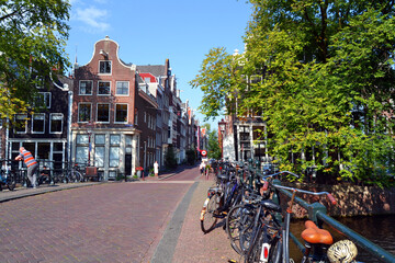 Traditional dutch architecture, facades of houses in Amsterdam, canal, bridge and bicycle parking. The Netherlands in summer time.

