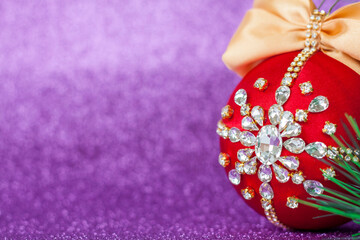 Red Christmas ball in rhinestones for Christmas tree decoration. Christmas toy. Christmas toy for decorating a Christmas tree on a lilac background. Shining crystals on a red ball.