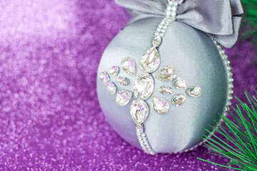 Grey Christmas ball in rhinestones for Christmas tree decoration. Christmas toy. Christmas toy for decorating a Christmas tree on a lilac background. Shining crystals on a gray ball.