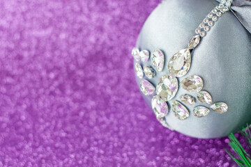Grey Christmas ball in rhinestones for Christmas tree decoration. Christmas toy. Christmas toy for decorating a Christmas tree on a lilac background. Shining crystals on a gray ball.