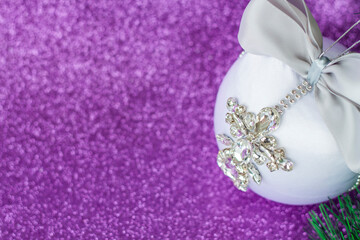 White Christmas ball in rhinestones for Christmas tree decoration. Christmas toy. Christmas toy for decorating a Christmas tree on a lilac background. Shining crystals on a white ball.