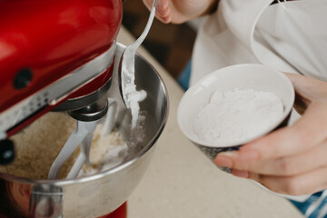 A close photo of powdered sugar is falling from the spoon into the stainless steel bowl of the red stand mixer which is mixing shortcrust pastry.