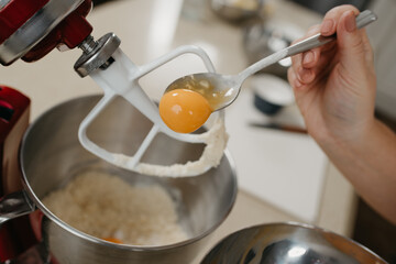 A close photo of the yolk is sliding from the spoon into the stainless steel bowl of the red stand mixer with shortcrust pastry.