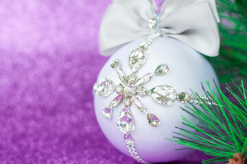 Obraz na płótnie Canvas White Christmas ball in rhinestones for Christmas tree decoration. Christmas toy. Christmas toy for decorating a Christmas tree on a lilac background. Shining crystals on a white ball.