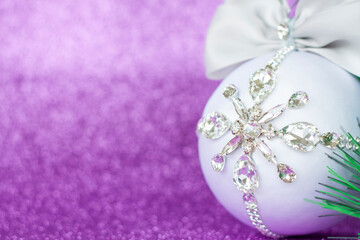 White Christmas ball in rhinestones for Christmas tree decoration. Christmas toy. Christmas toy for decorating a Christmas tree on a lilac background. Shining crystals on a white ball.