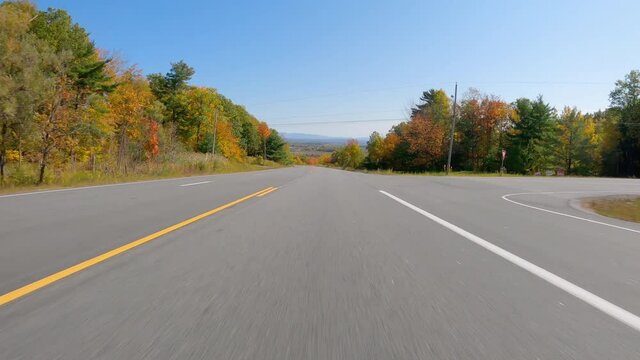 POV Driving a car going down on asphalt road with multi color trees in fall season. Sunny day with blue sky 