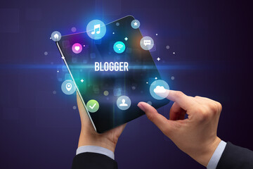 Businessman holding a foldable smartphone with BLOGGER inscription, social media concept