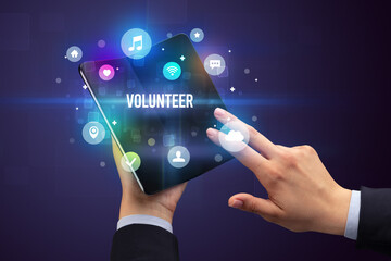 Businessman holding a foldable smartphone with VOLUNTEER inscription, social media concept