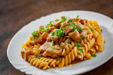 Sliced fried chicken fillet in a creamy sauce with fusilli pasta in white plate on wooden table