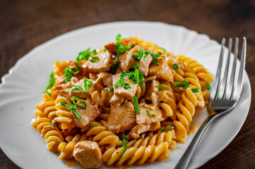 Sliced fried chicken fillet in a creamy sauce with fusilli pasta in white plate on wooden table