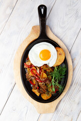 Austrian cuisine: fried potatoes with meat, ham and eggs in a pan close-up.